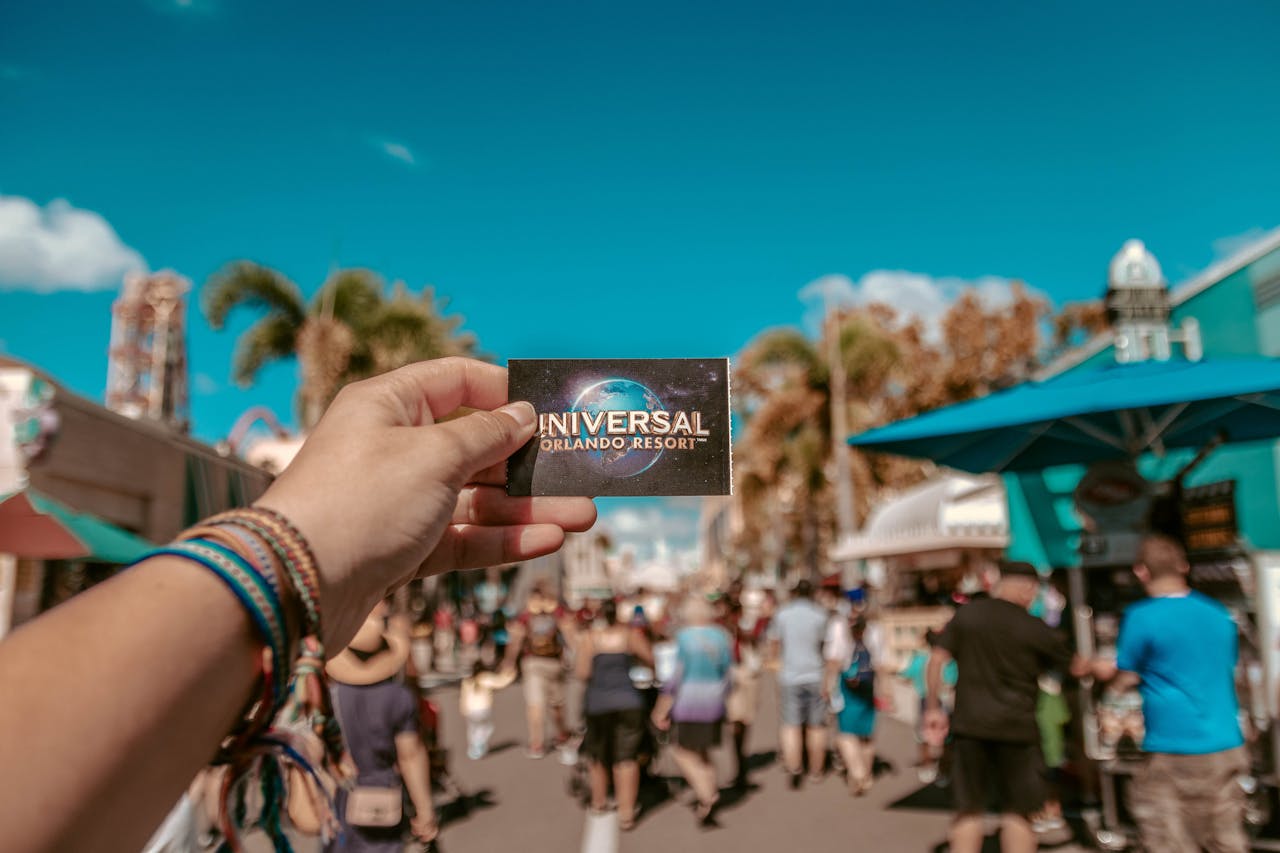creative-02 A hand holding a Universal Orlando Resort ticket in a bustling theme park setting.