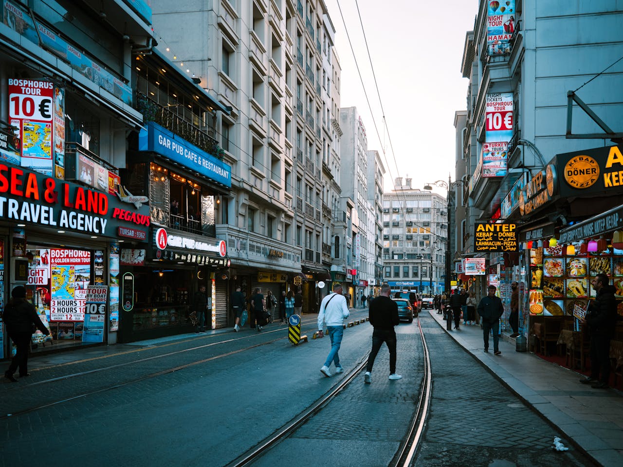 creative-03 Vibrant street scene in Istanbul featuring shops, people, and tram tracks under a clear sky.